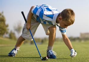 A young golfer bends over to tee up a ball